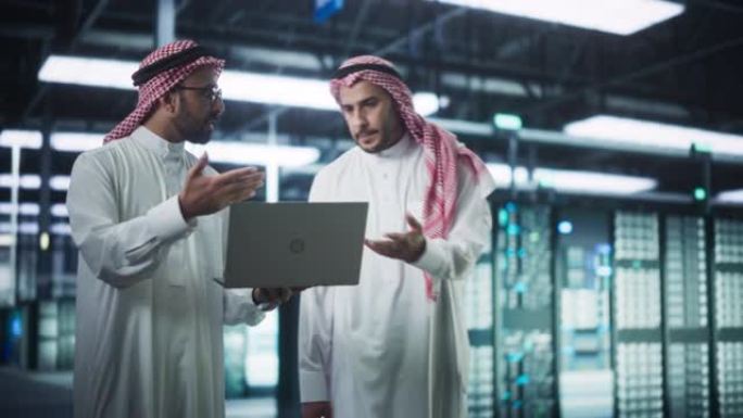 中东计算机工程师和网络安全专家在服务器机房工作，与笔记本电脑交谈，进行系统维护检查。在数据中心做数据