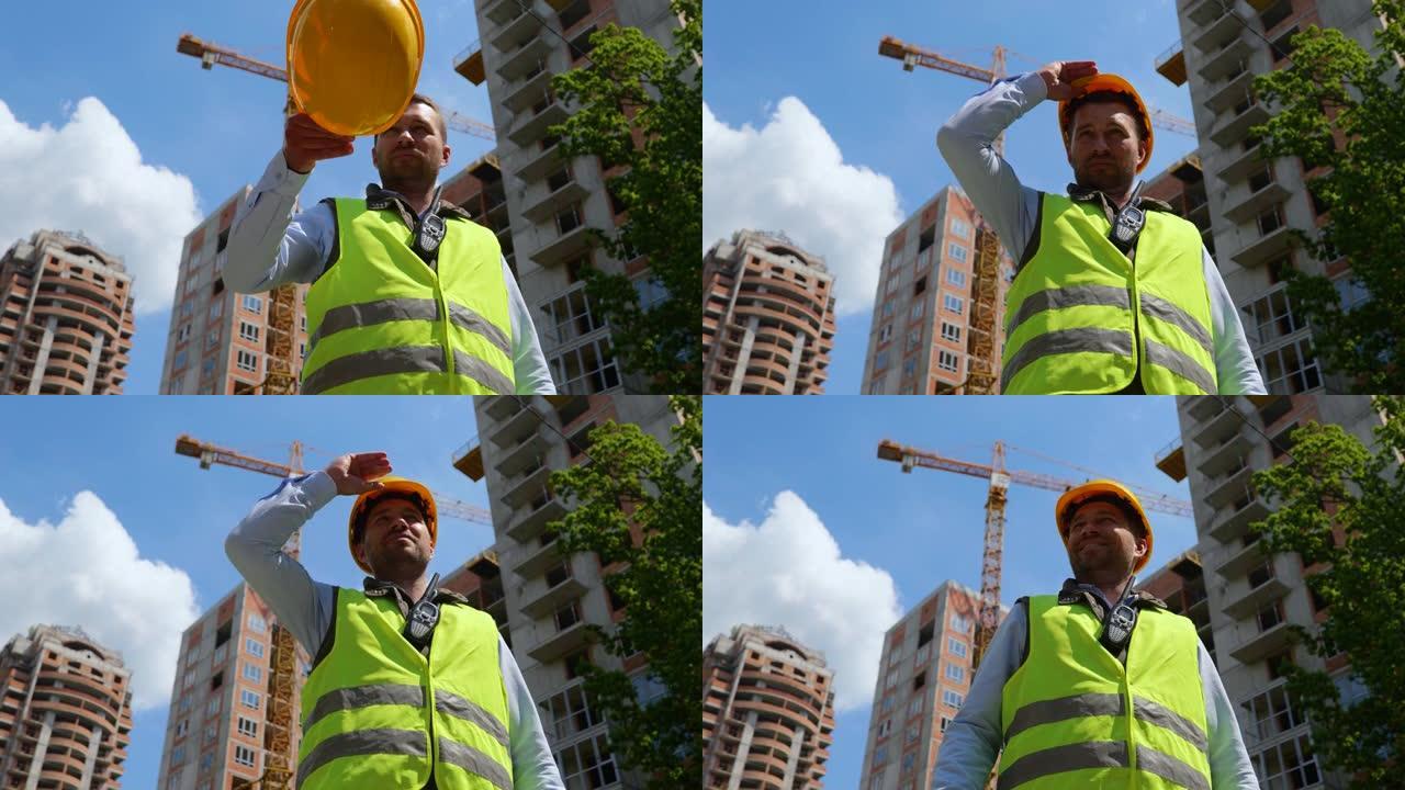 微笑的工人戴着安全帽，站在街上，背景是一栋未完成的建筑。工业建设、工程和建筑概念