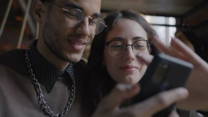 在咖啡馆约会期间，快乐的混血儿夫妇一起使用智能手机聊天享受社交媒体
