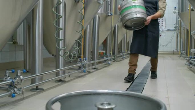 年轻的男工人在啤酒厂携带空啤酒桶