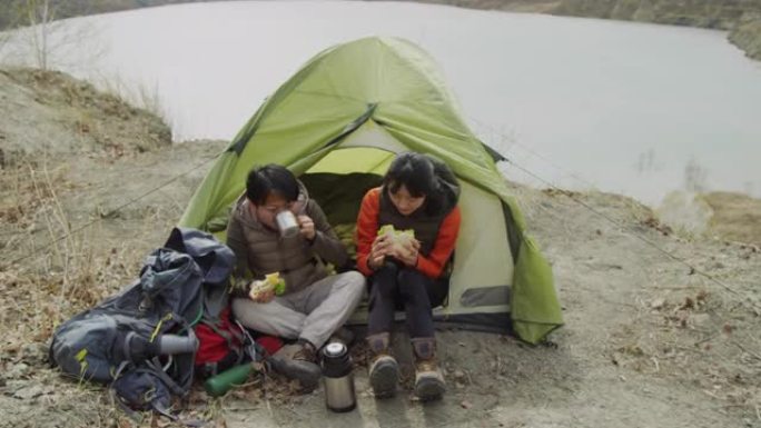 两名亚洲女性游客在风湖海岸的帐篷入口旁吃午餐
