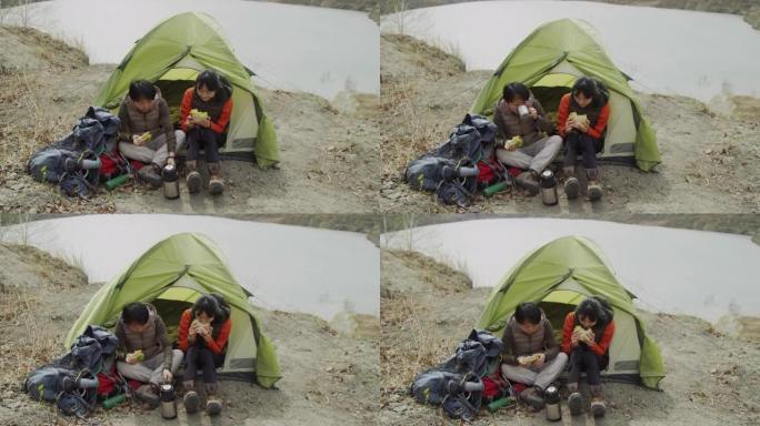 两名亚洲女性游客在风湖海岸的帐篷入口旁吃午餐