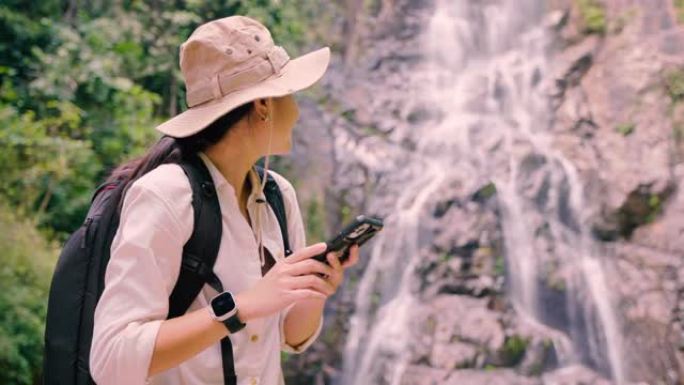 亚洲女孩徒步旅行用手机拍照瀑布。