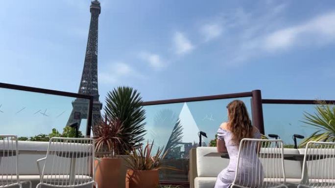 一个年轻女孩背坐在俯瞰埃菲尔铁塔的餐厅里，风吹着她的头发。餐馆和旅游经营者有广告和文字的地方。
