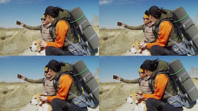 两名游客与狗坐在斜坡边缘制作视频的侧视图