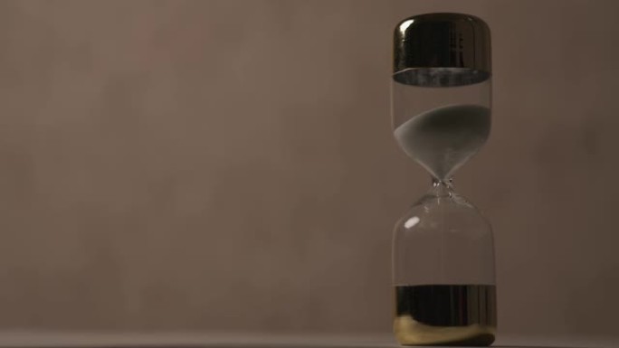 沙漏说明了时间耗尽的概念作为一个计时器，时间在棕色背景前滴答作响