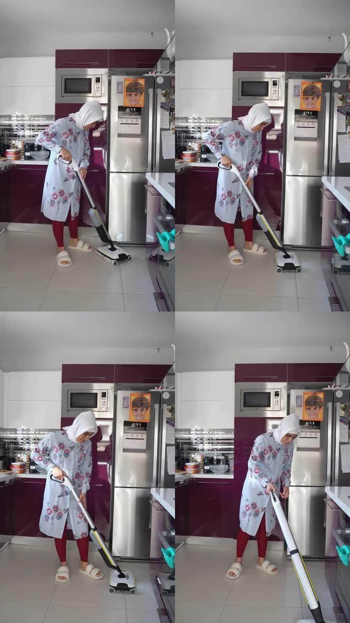中年穆斯林妇女在厨房戴着头巾的无线吸尘器地板上吸尘。家庭主妇用电子设备清洁洗涤家庭。家电技术在日常生