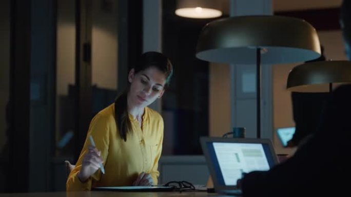 商务女性在办公室工作到很晚，坐在办公桌前检查智能手机头脑风暴想法浏览数字平板电脑技术