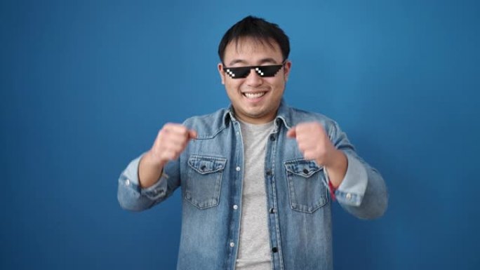 戴着暴徒生活眼镜的中国年轻人在孤立的蓝色背景上扔美元