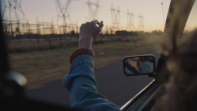 年轻女子在车里牵着手走出窗户，感觉风从手指吹过，在乡村公路旅行中开车去暑假旅行，享受日落时在路上的自