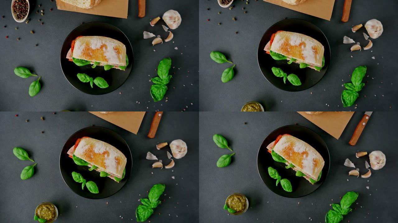 夏巴塔三明治，火腿，香蒜酱，西红柿，黑色背景上的罗勒。食品。食物背景。顶视图