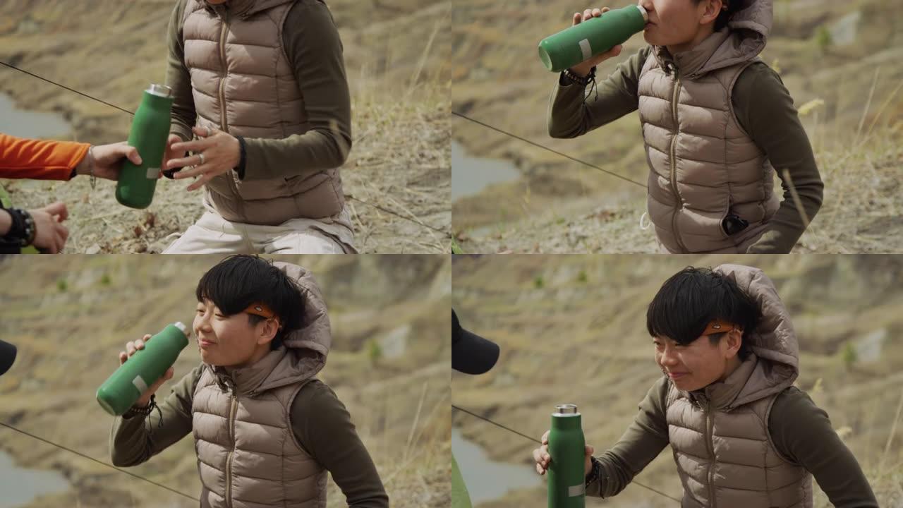亚洲女性游客从她的朋友那里拿热水瓶，喝酒，远足湖岸