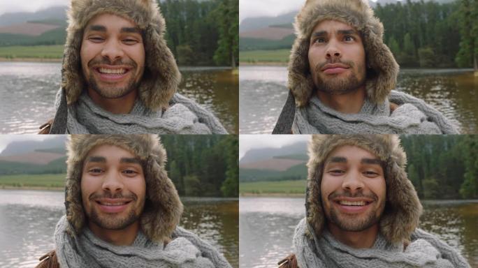 画像有吸引力的年轻男子微笑快乐，滑稽的面孔，戴着毛皮帽子在大自然的湖边户外