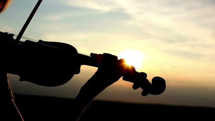 剪影女孩小提琴手在日落时拉小提琴。特写。