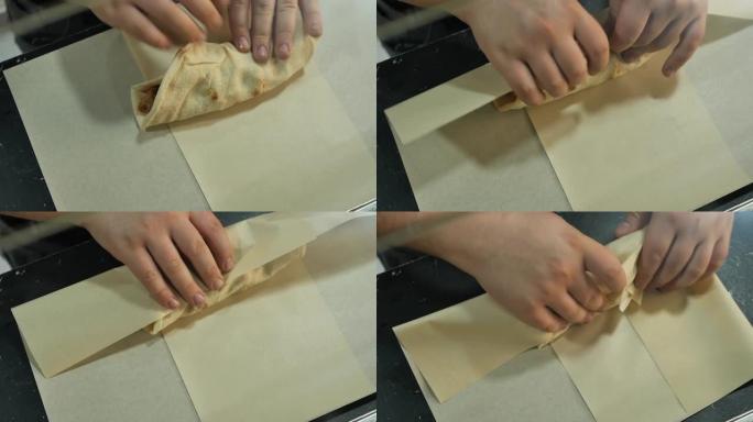 库克将煮熟的沙威玛用包装纸包起来。厨师的手把烤肉串放在纸上，打包给买家。送餐和外卖。顶视图