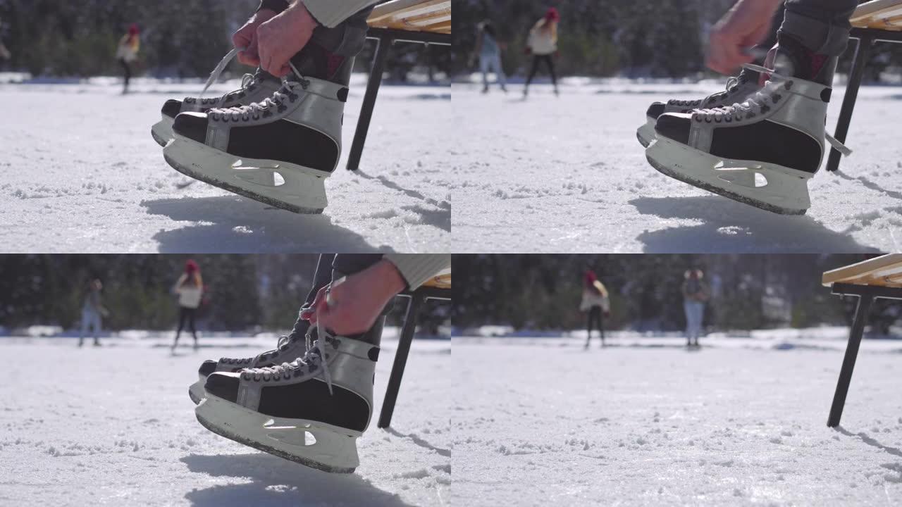 LD人坐在冰冻的湖面上的长凳上，将鞋带绑在冰刀上