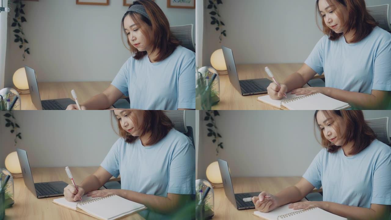 专注的亚洲女性坐在办公桌前，用笔记本电脑在网上学习笔记。教育网络研讨会课程，电子学习。