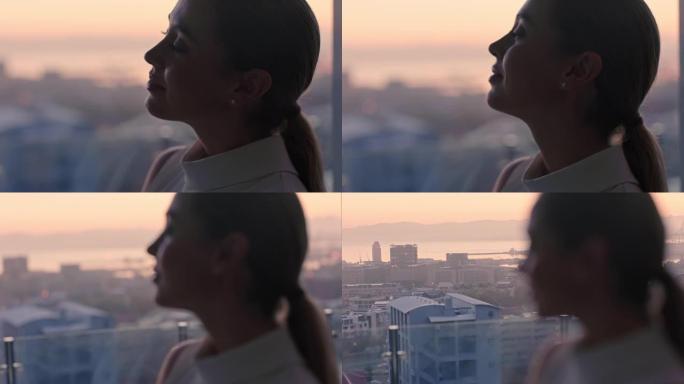 美丽的女商人看着窗外，思考着成功的生活方式规划，在日落时从顶层公寓欣赏城市的景色