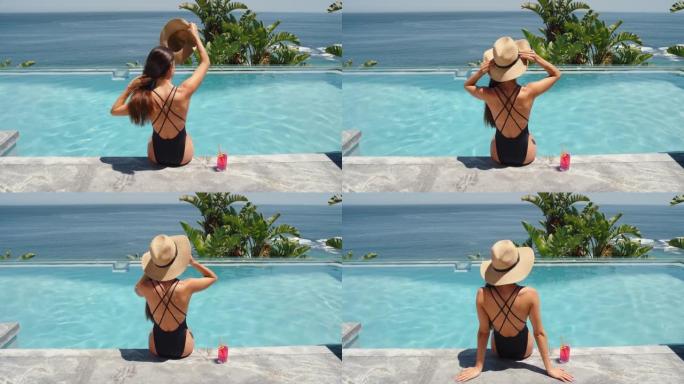 坐在游泳池边喝酒的旅行女人在豪华酒店度假村享受美丽的海景，棕榈树戴着帽子4k