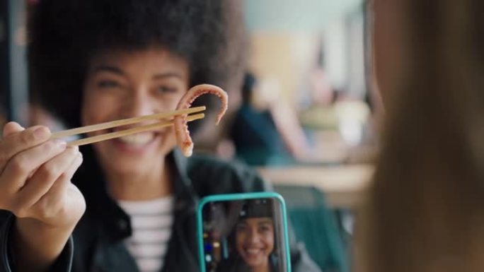 年轻的非洲裔美国妇女在餐厅吃海鲜，展示最好的朋友使用智能手机拍摄奇怪的食物的照片朋友在社交媒体上一起