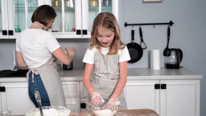 和女儿一起做饭，可爱的女孩子准备糕点面团，并用面粉拍手，妈妈手里拿着牛奶