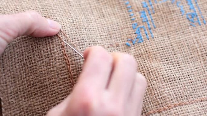 POV手在粗麻布织物上缝制米色线和针的链式针迹