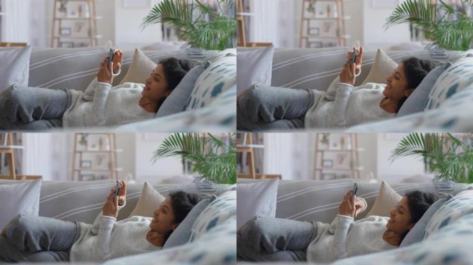 非裔美国妇女使用智能手机在沙发上放松发短信浏览社交媒体信息在家享受手机4k镜头