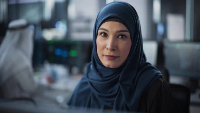 中东女性的肖像使用台式计算机，看着相机并微笑着。授权穆斯林信息技术专家，软件工程师，开发人员或数据科