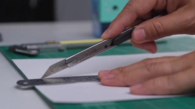 使用美工刀切纸的女性特写手。女性用刀用尺子在切割垫上切纸。