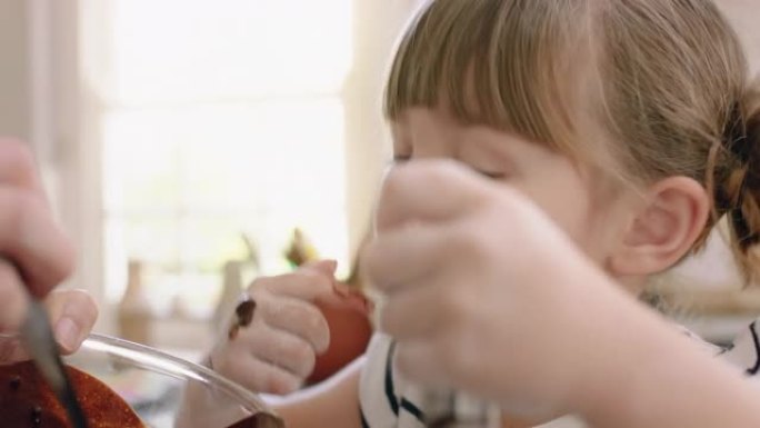 快乐的小女孩帮助妈妈在厨房烘烤，有趣地将配料与妈妈在家准备食谱混合