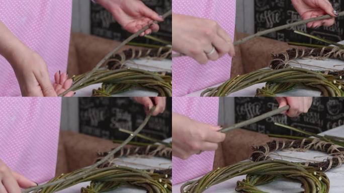 一个女人手里拿着藤蔓的树枝来编织。藤蔓编织的花环躺在桌子上。不同的尺寸。附近的藤蔓树枝。特写。