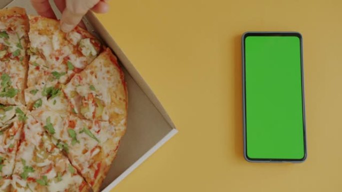 从绿屏色度键智能手机旁边的盒子里手工拿比萨饼的俯视图