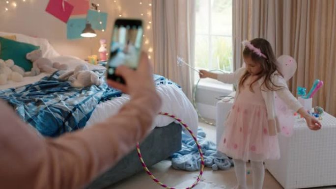 快乐的小女孩在卧室里穿着童话装扮，母亲在社交媒体上使用智能手机分享拍照