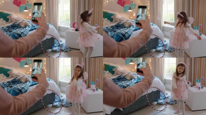 快乐的小女孩在卧室里穿着童话装扮，母亲在社交媒体上使用智能手机分享拍照