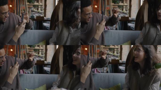 年轻人的慢动作使用智能手机在咖啡馆里玩乐给女友拍照