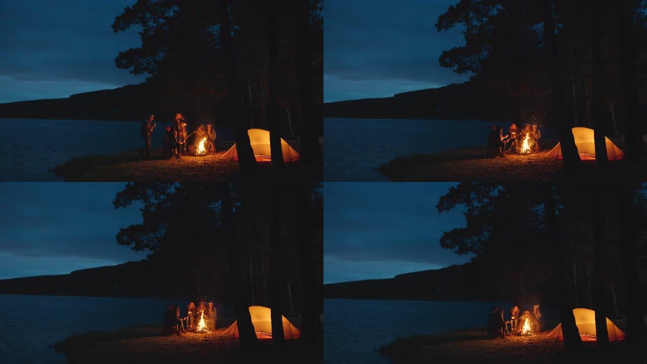 一群朋友坐在篝火旁烤棉花糖在湖边的森林里露营，晚上聊天分享温暖享受户外冒险4k