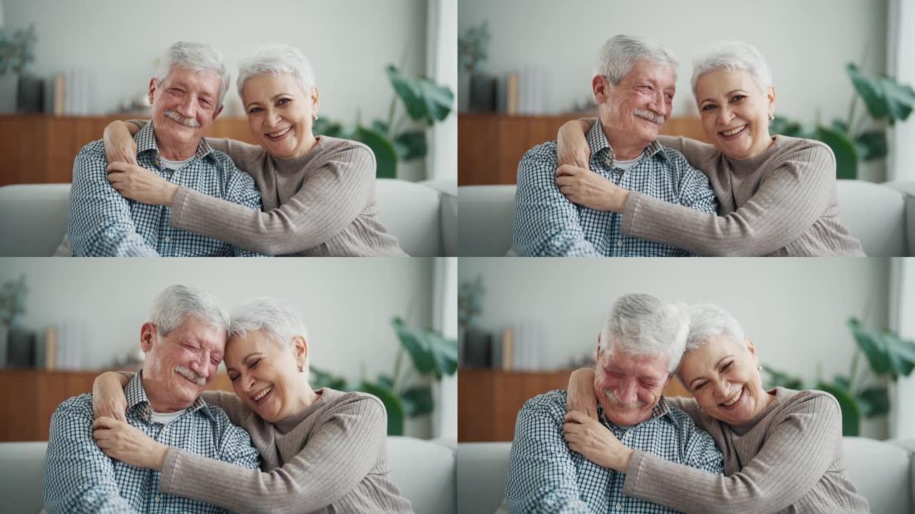 老年夫妇的肖像拥抱坐在家里的客厅沙发上，老年妻子和丈夫在一生的关系中，幸福的婚姻观念。白发苍苍的老人
