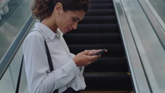 混合种族商务女性使用智能手机上网浏览女性通勤者在自动扶梯上出差在办公室步行地铁大厅4k