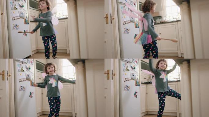 快乐的小女孩戴着可爱的仙女翅膀在厨房跳舞，挥舞着勺子玩得开心，假装做有趣的舞蹈动作，享受周末在家
