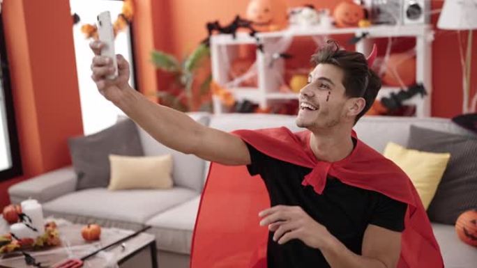 穿着魔鬼服装的年轻西班牙裔男子在家中通过智能手机进行自拍