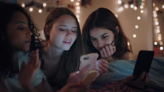 快乐的少女躺在床上，使用智能手机浏览社交媒体短信分享八卦享受周末的睡眠