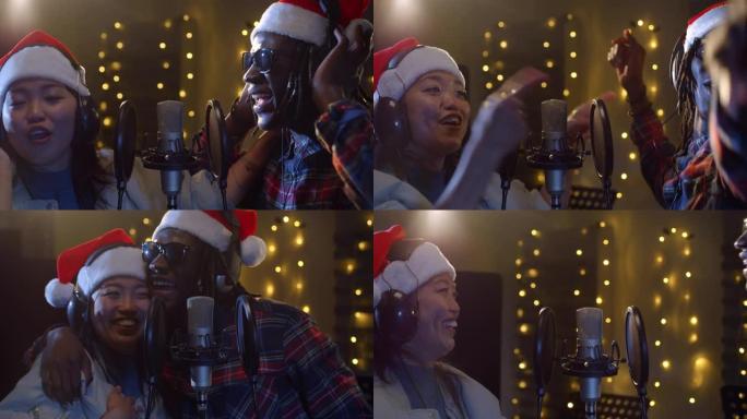 在录音棚里用圣诞老人帽子录制的两位不同歌手的特写肖像。年轻的黑人男性和亚洲女性艺术家为圣诞节唱歌，合