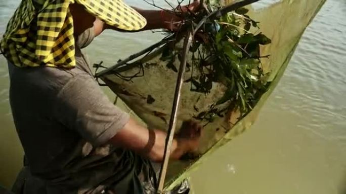 对虾渔夫捕捉虾，诱饵网并将其推入河中更深的上部特写视图
