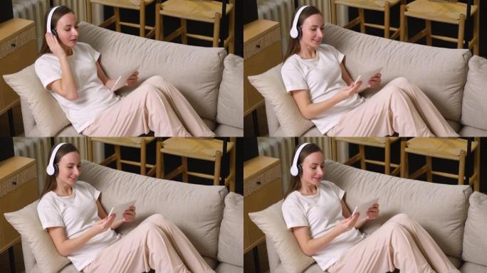 一个戴着耳机的迷人女人喜欢坐在沙发上在平板电脑上看电影