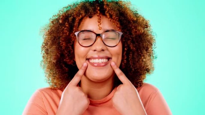 脸，黑人女人，指着嘴，微笑和幸福在蓝色的工作室背景下。肖像，牙买加女性和女士展示牙齿，美白和幸福，充
