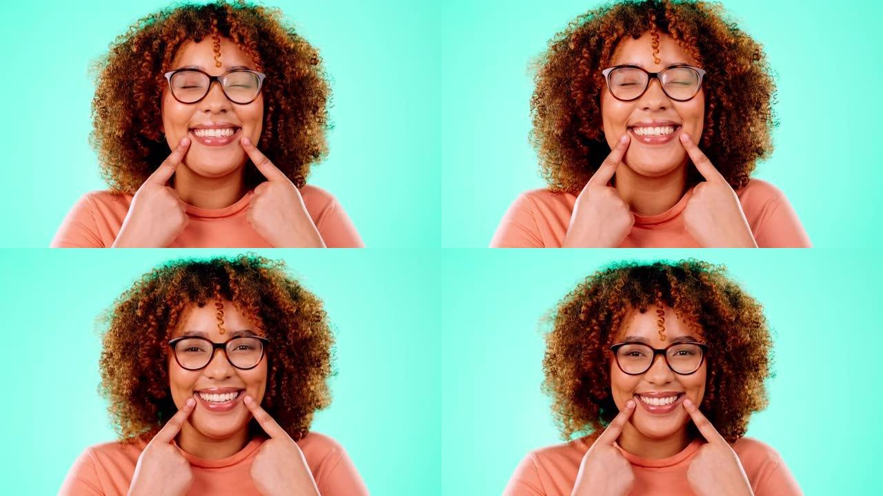 脸，黑人女人，指着嘴，微笑和幸福在蓝色的工作室背景下。肖像，牙买加女性和女士展示牙齿，美白和幸福，充