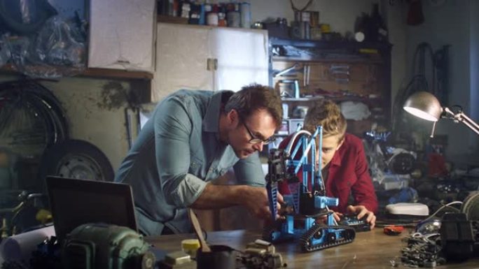 十几岁男孩的肖像和他的父亲一起在家庭车间的学校为工程项目建造机械臂原型。男人和儿子对机器人技术的热情
