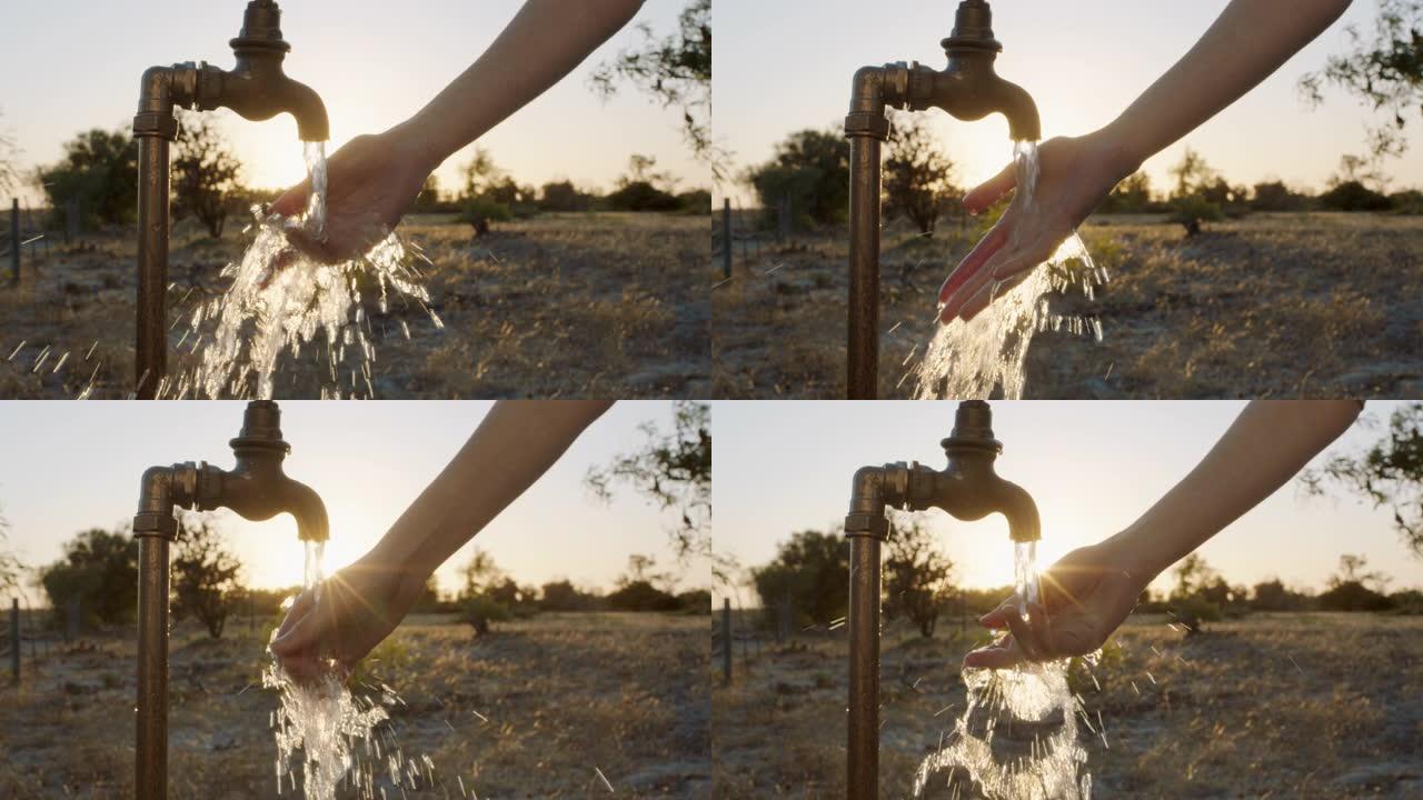 女人在日落时分在农村农场的水龙头下洗手从水龙头流出的淡水