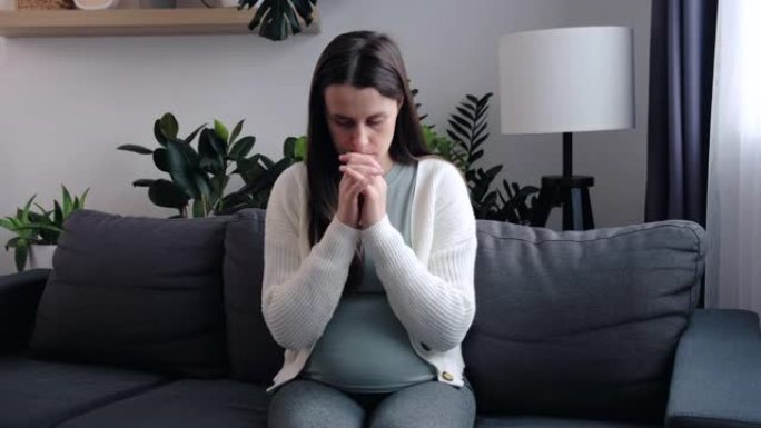 担心的年轻白人孕妇独自坐在家里的沙发上时会感到压力和焦虑。准妈妈正在考虑即将出生的孩子。抑郁与母性概