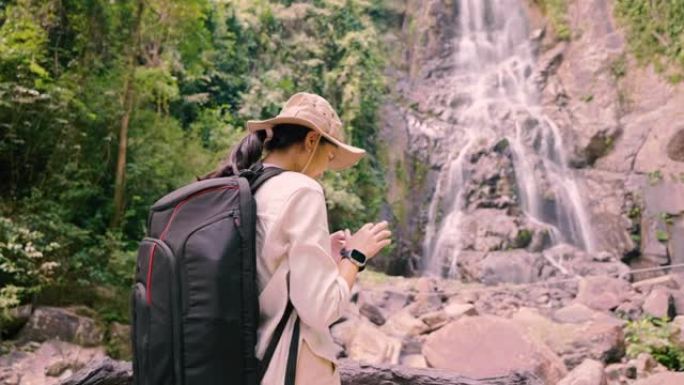 亚洲女孩徒步旅行用手机拍照瀑布。